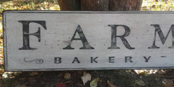 Farmhouse Bakery wood Sign laying against a tree.