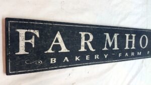 Close-up of a rustic distressed black farmhouse sign with off white lettering.