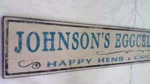 Close-up of the Johnsons Happy Hens and Chickens wood sign in teal lettering