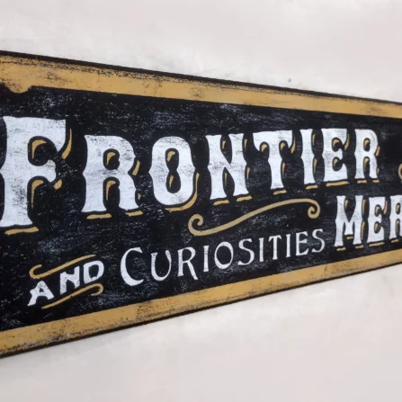Closeup view of the antique style wood sign showing off-white letters and gold accents on a black background.