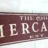 Closeup view of off-white letters on a rustic burgundy mercantile sign