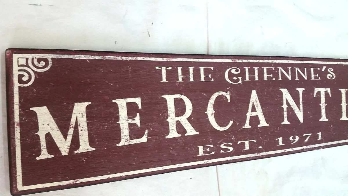 Closeup view of off-white letters on a rustic burgundy mercantile sign