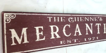 Closeup view of off-white letters on a rustic burgundy mercantile sign