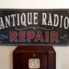 An antique style Radio Repair sign sitting on top of an old radio.