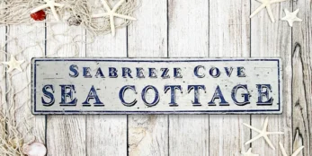 Antique-style Sea Cottage sign with distressed white background and navy blue letters