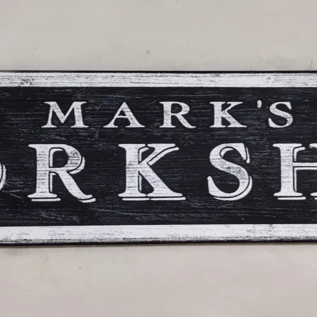 Antique style workshop sign with black background and white lettering, featuring elegant decorative design.